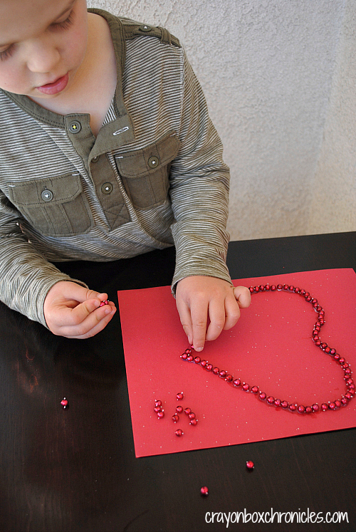 Child glueing red loose parts onto heart