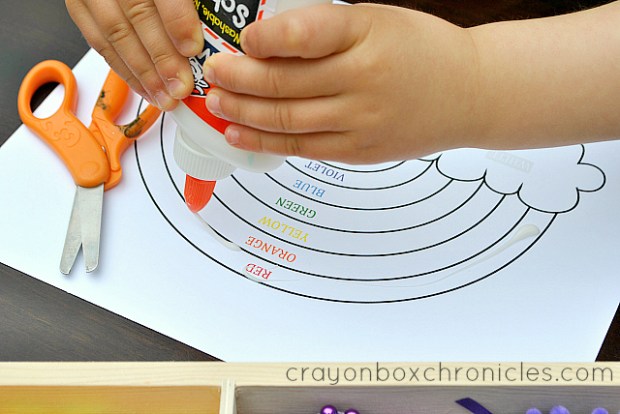 child adding glue to rainbow sensory collage